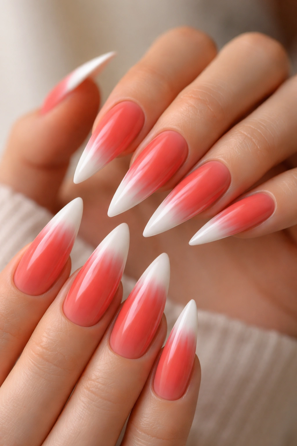 Close-up of coral-red ombré stiletto nails with white French tips, glossy manicure.