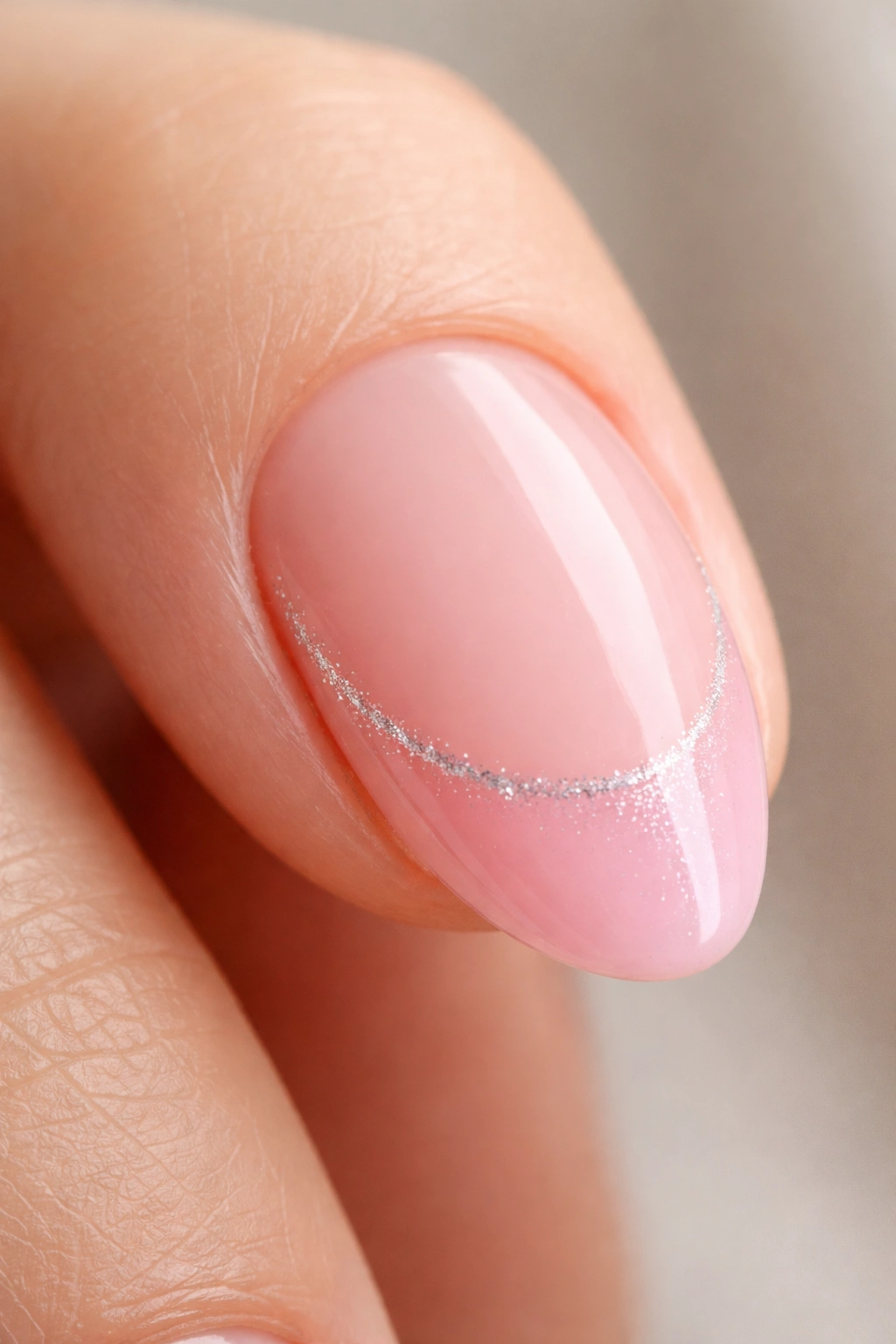 Close-up of a short almond nail with a cotton candy pink tip and a thin glitter seam