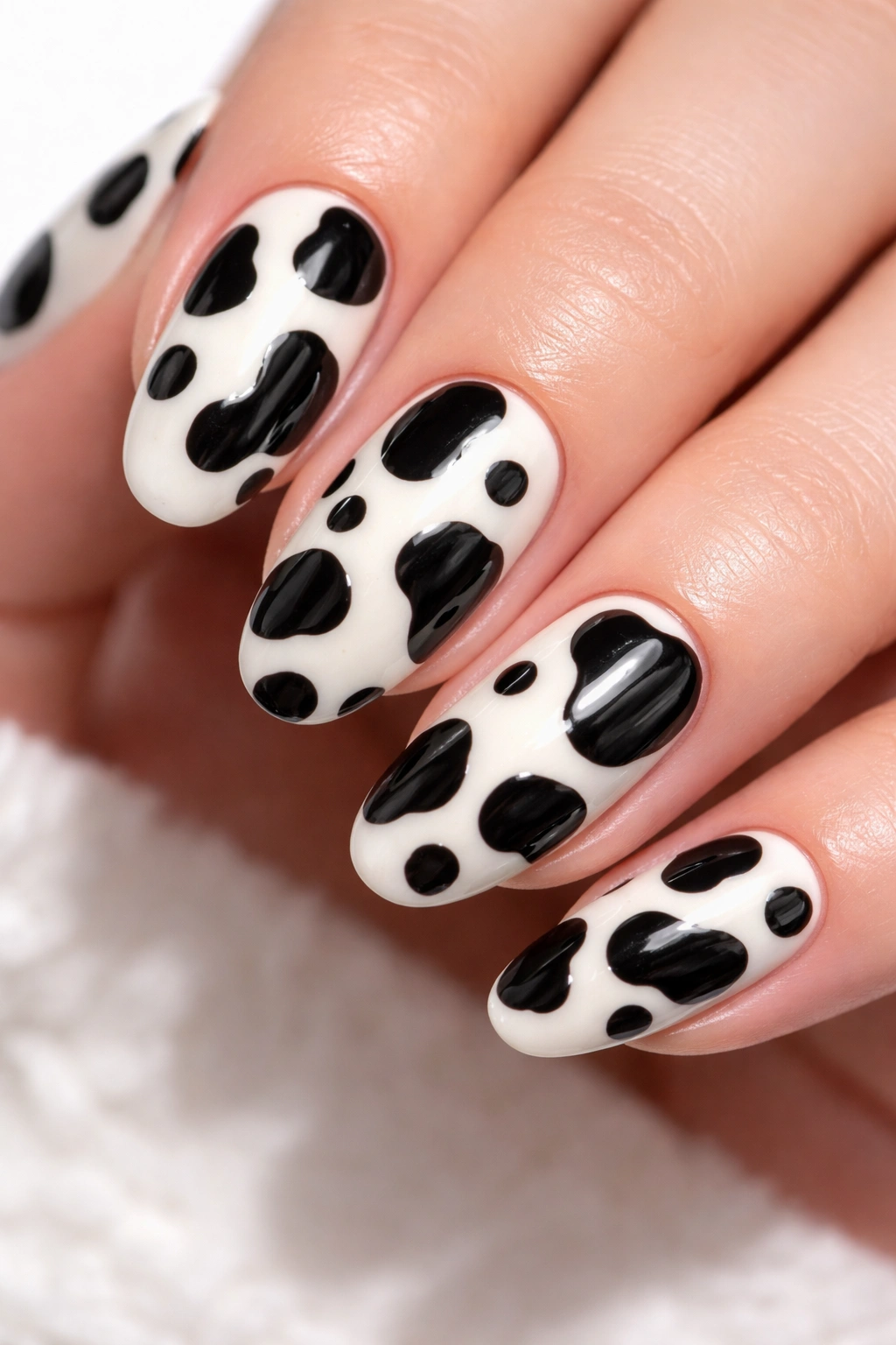Close-up of cow print nail design with black patches on white background.
