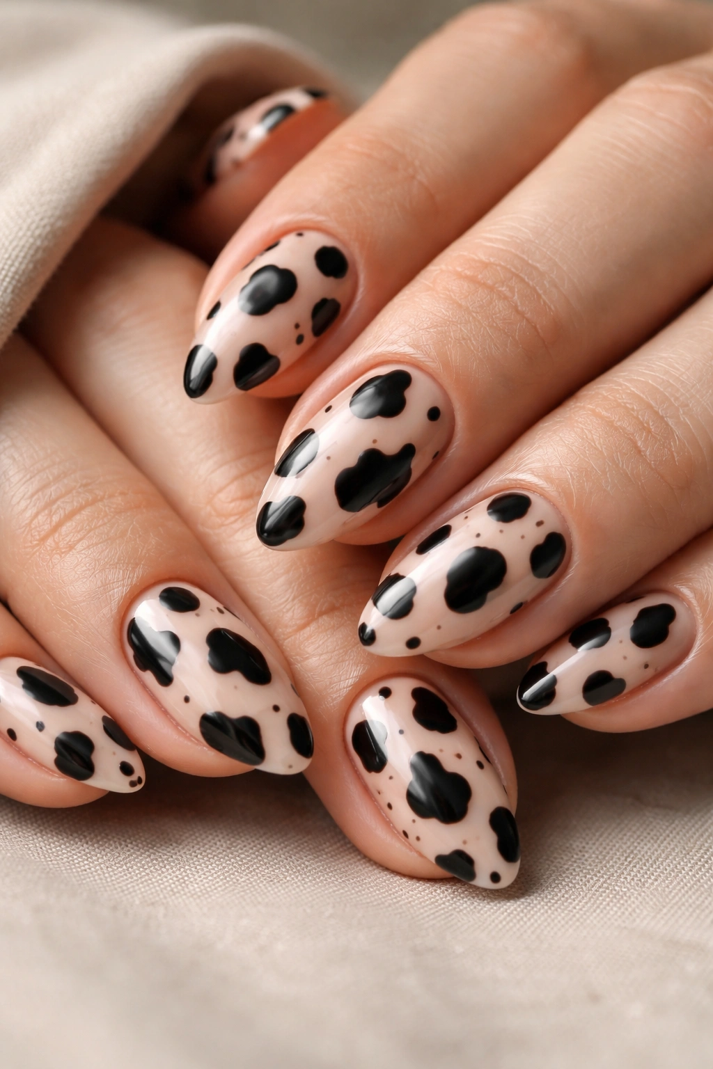 Close-up of short almond cow print nails with irregular spots and edge breathing room, glossy finish