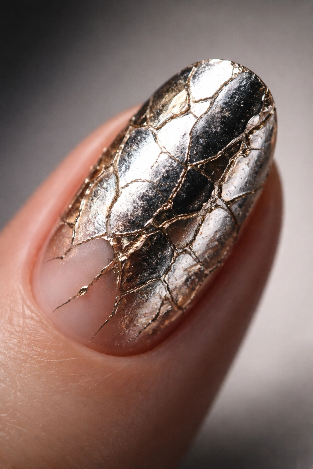Close-up of a fingernail with cracked metallic foil texture and chrome finish.