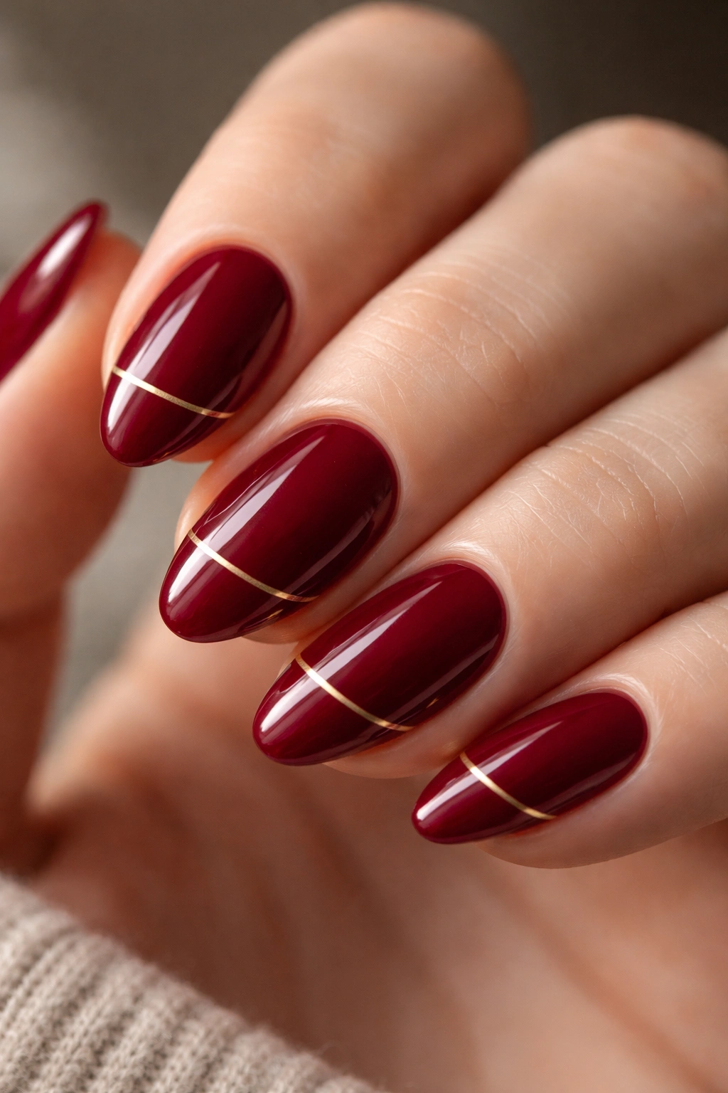 Cranberry red nails with a thin gold line on short almond nails