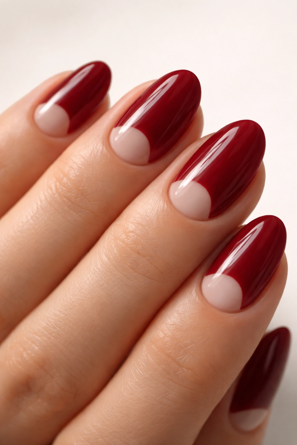 Close-up of short almond nails with cranberry red and negative-space crescent