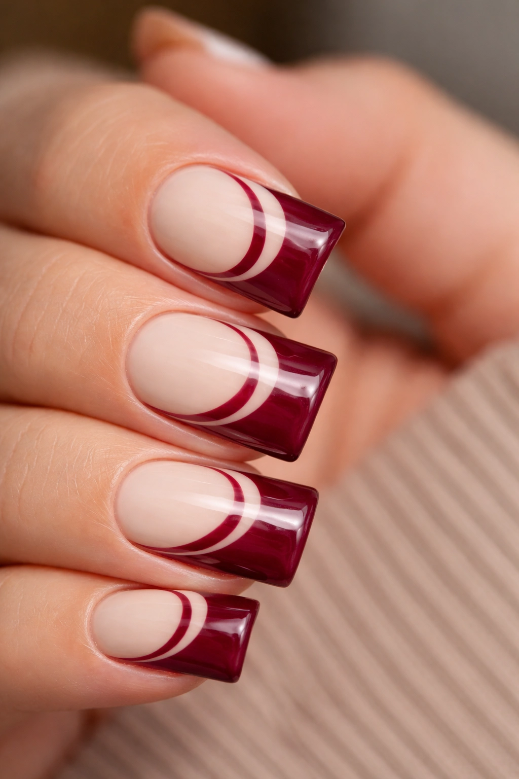 Close-up of a cream nail with burgundy duck tip and negative-space pattern