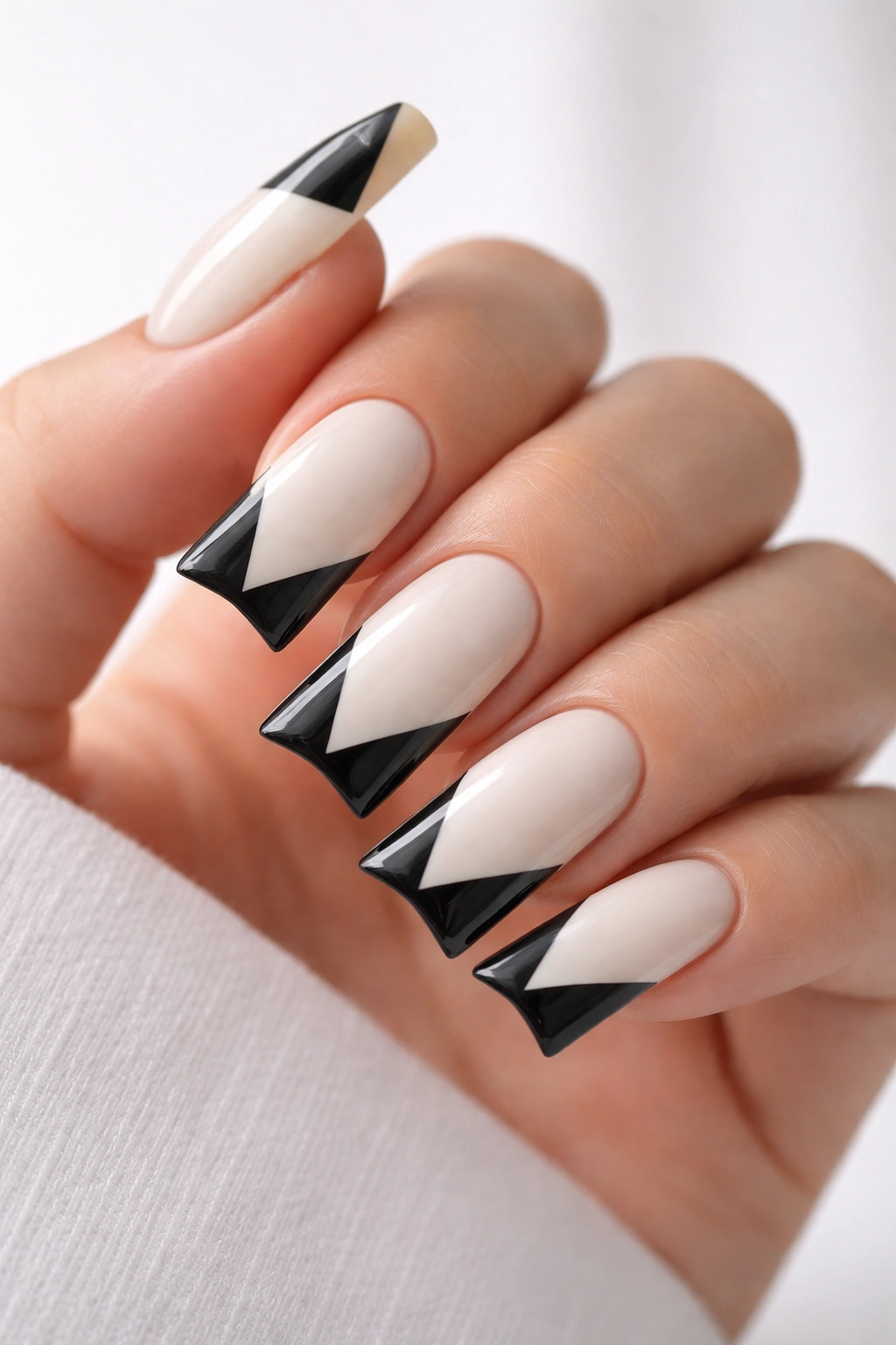 Close-up of duck nails with cream base and black geometric triangles.