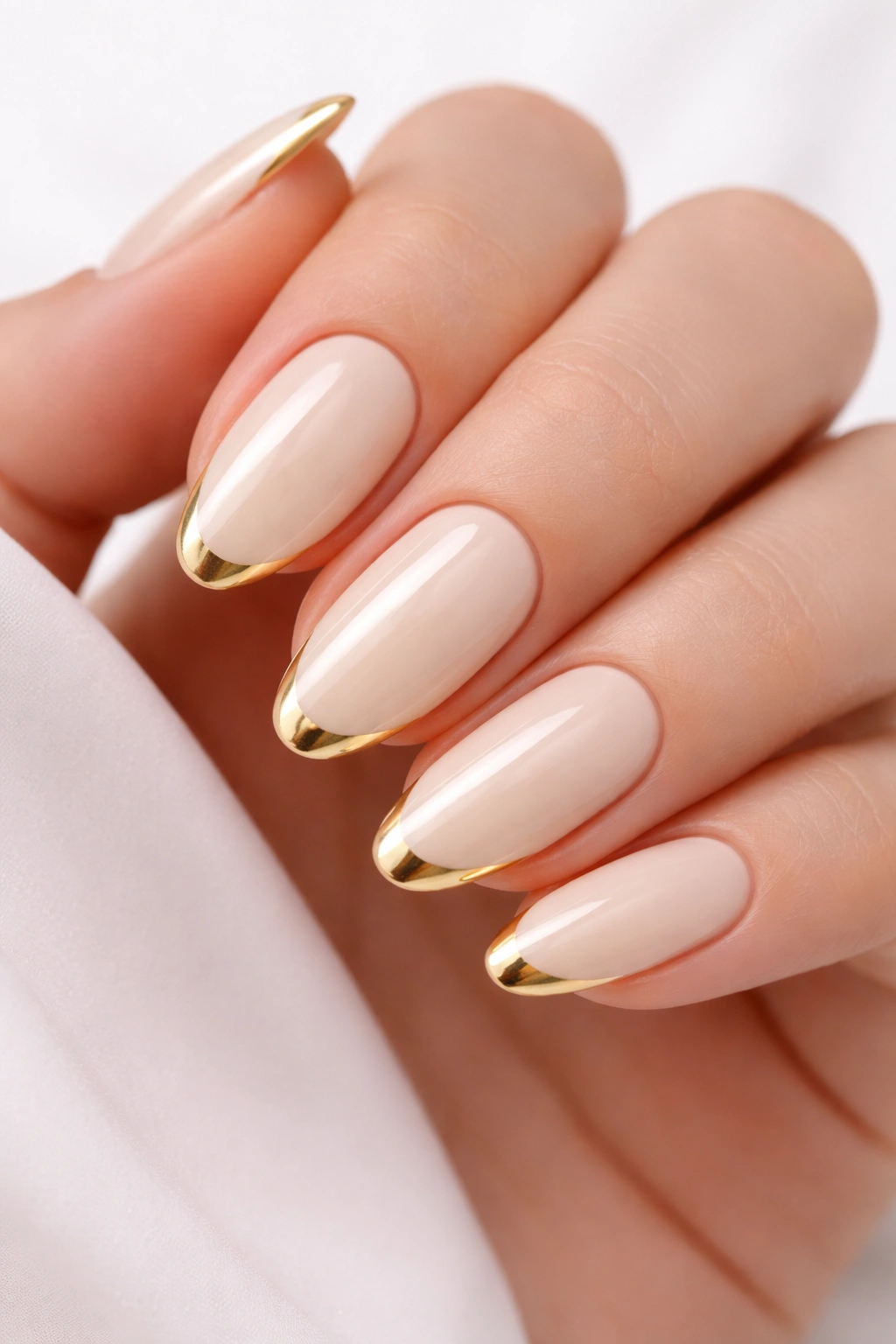 Close-up of nails with cream base and gold French tips on almond-shaped nails