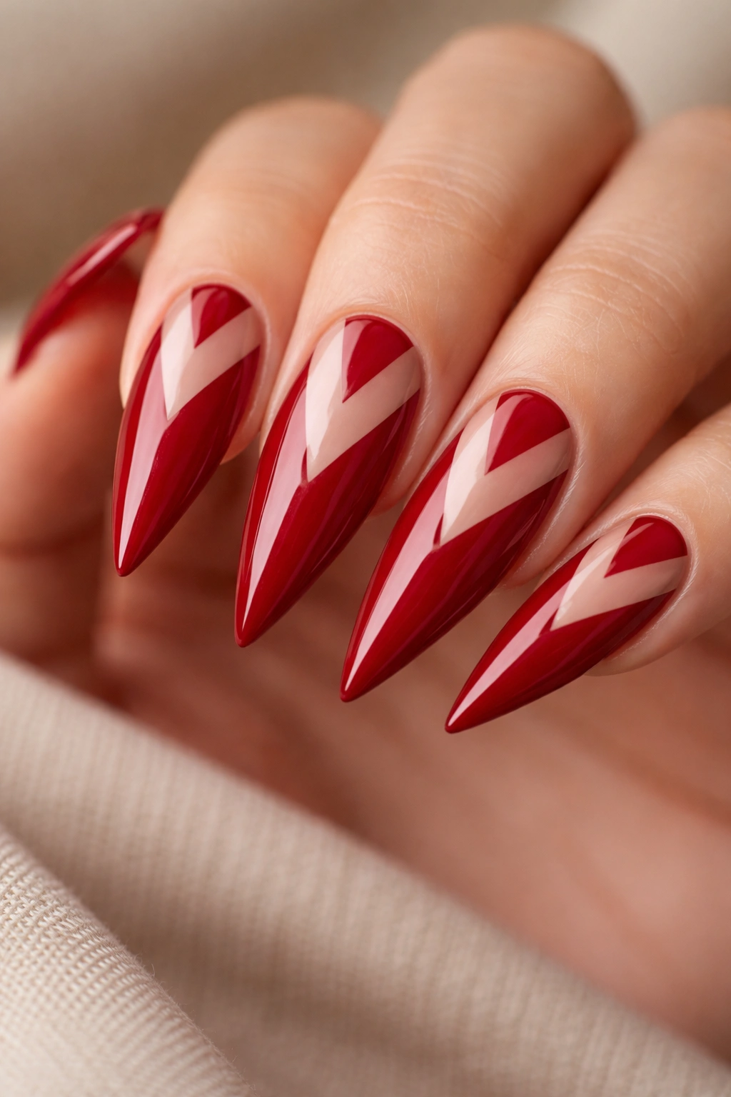 Crimson stiletto nails with negative-space chevron patterns.