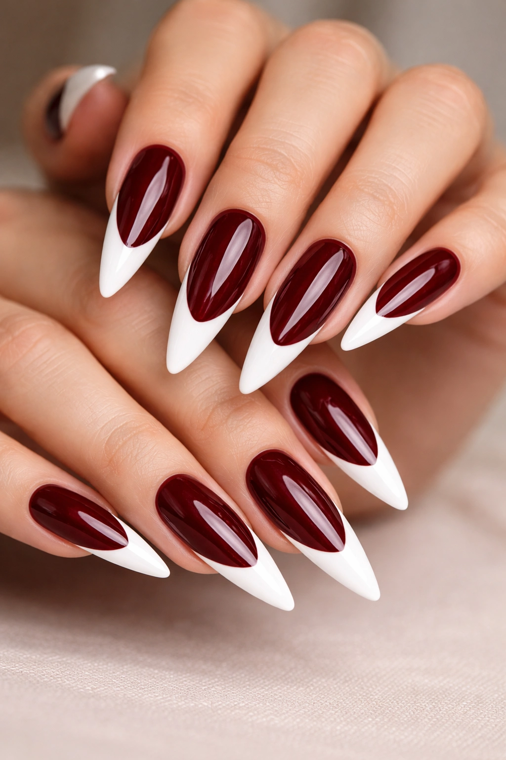 Close-up of dark burgundy stiletto nails with white tips and a glossy shine