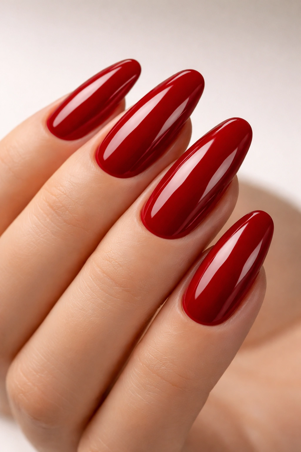 Close-up of long rounded nails painted glossy crimson red with mirror-like shine.