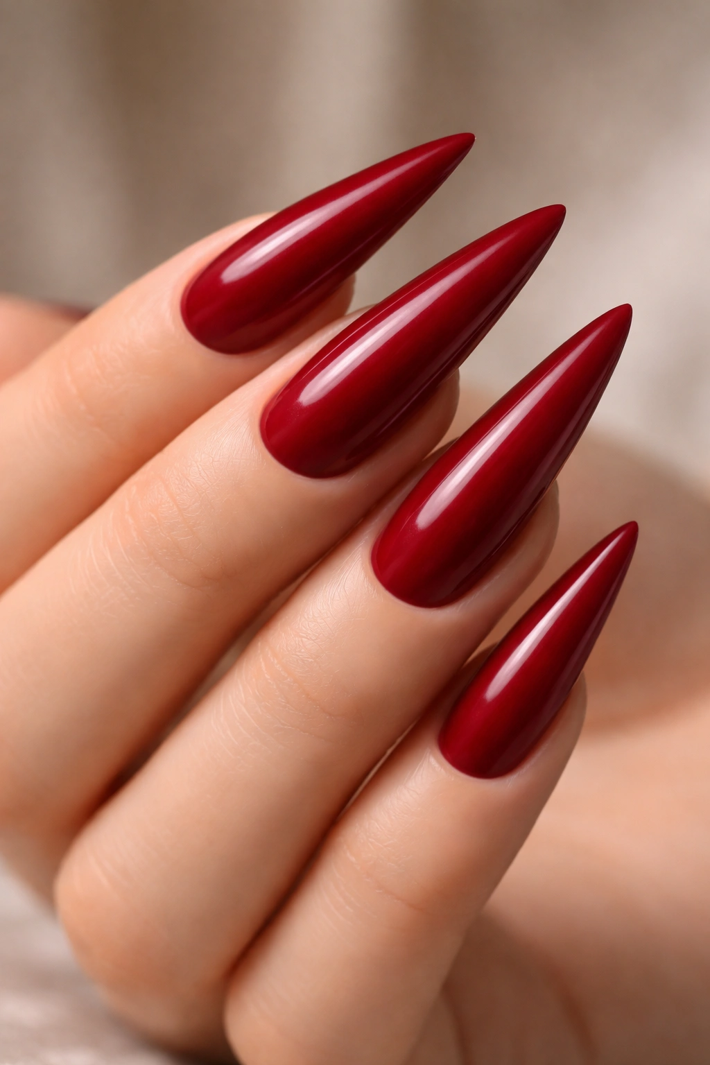 Close-up of deep crimson stiletto nails with a satin finish on a neutral background