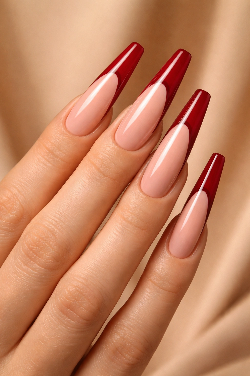 Close-up of long nails with crimson red French tips on nude base.
