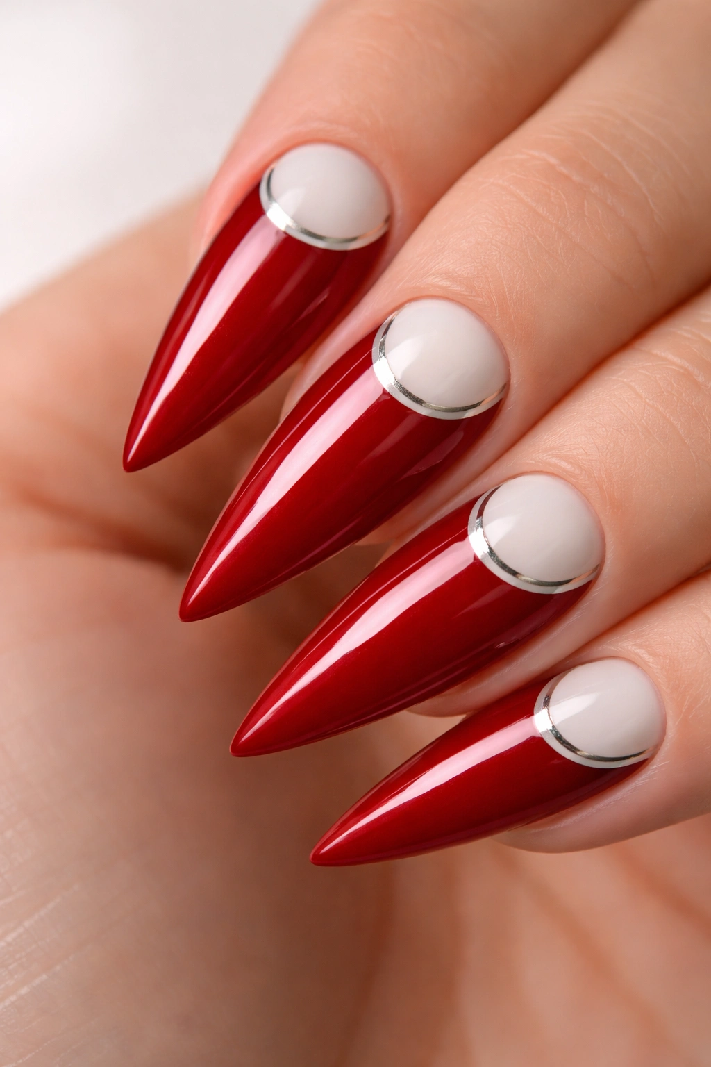 Close-up of crimson red stiletto nail with a curved white reverse French tip and metallic line