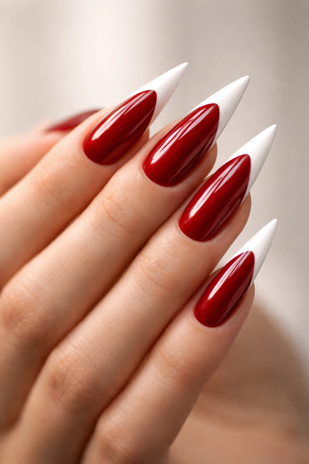 Close-up of stiletto nails with crimson base and white tips on a neutral background
