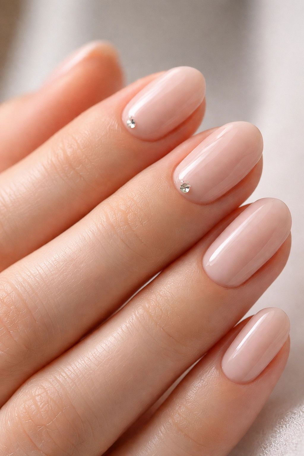 Close-up of short oval nails with a tiny crystal near the cuticle on a nude base