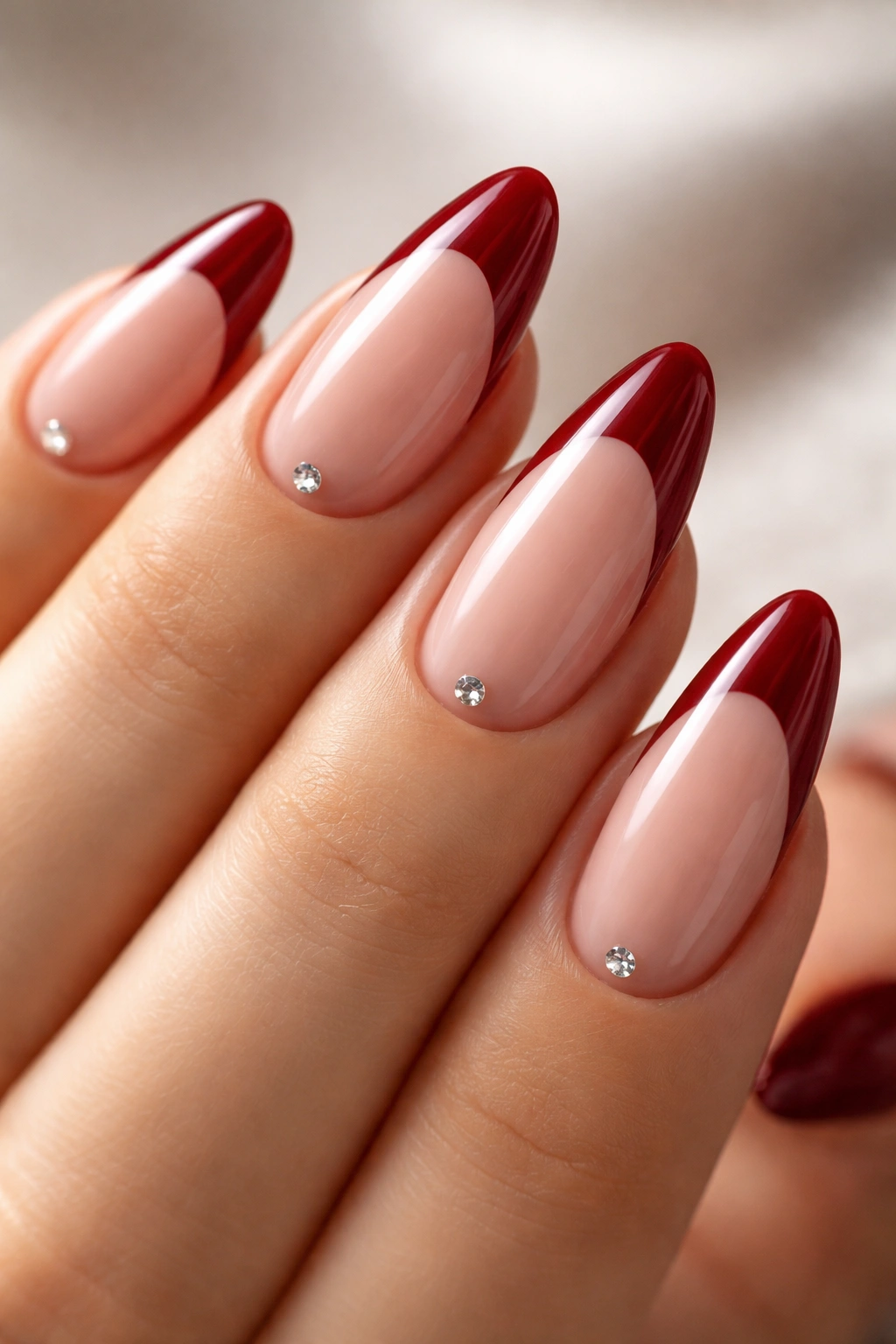 Almond nails with deep red tips and a single crystal near the cuticle