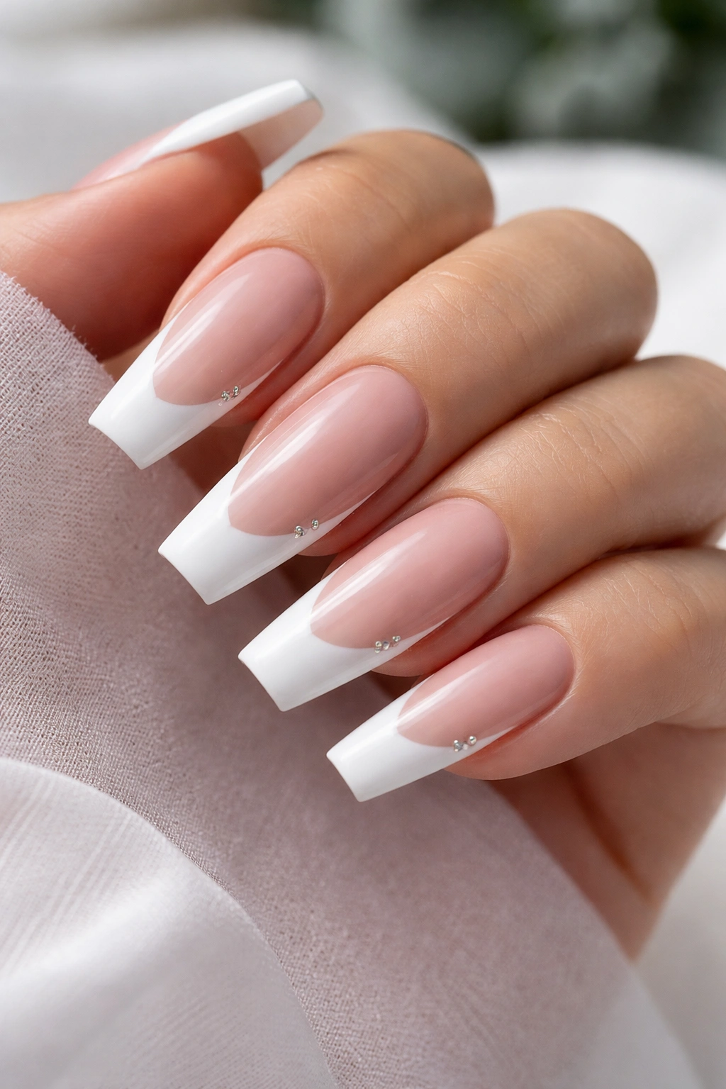 Close-up of white French tip ballerina nails with tiny crystal corners