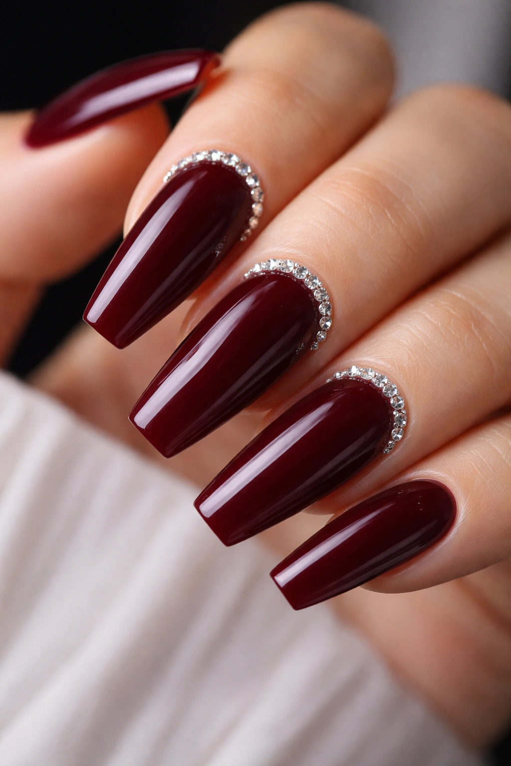 Nails with a delicate crystal arc along the cuticle on a deep red base.