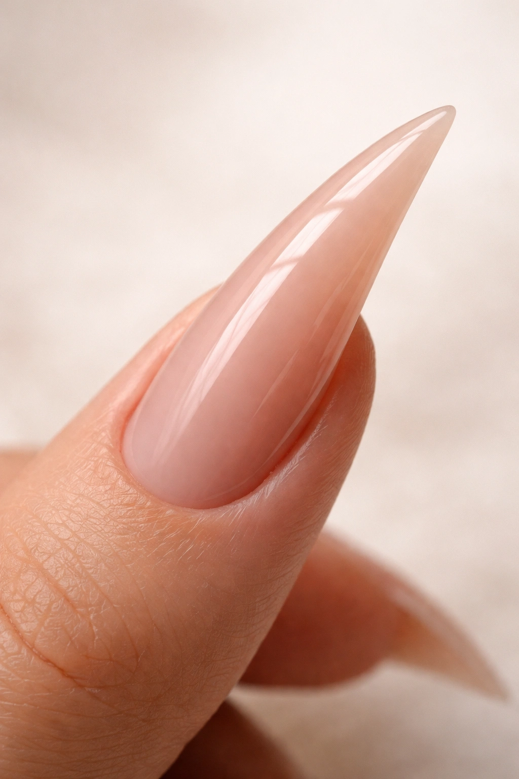 Close-up of a curved stiletto nail with a glossy nude finish and pronounced curve