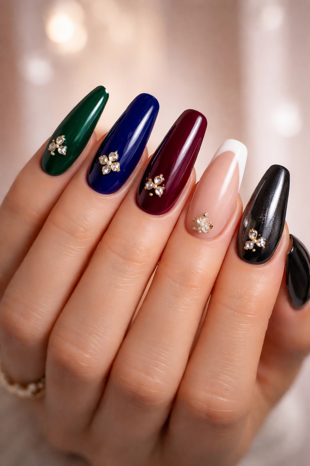 Hand with nails showing multiple design options in jewel tones and chrome