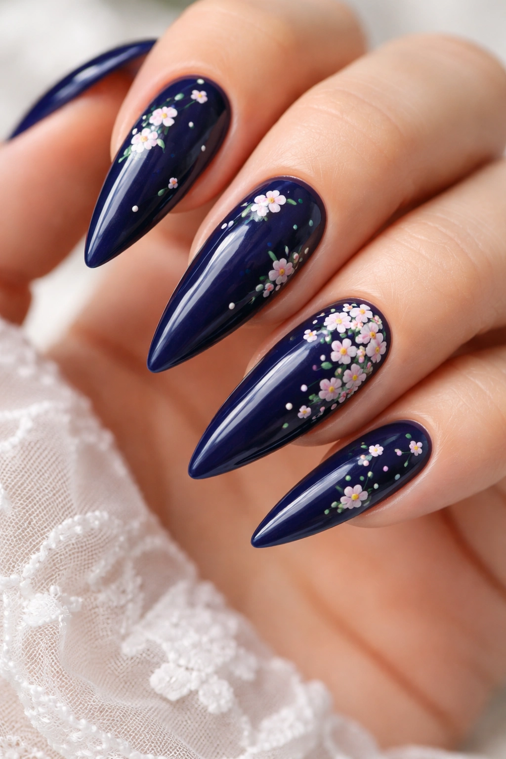 Close-up of dark blue stiletto nails with tiny white and pink floral designs.