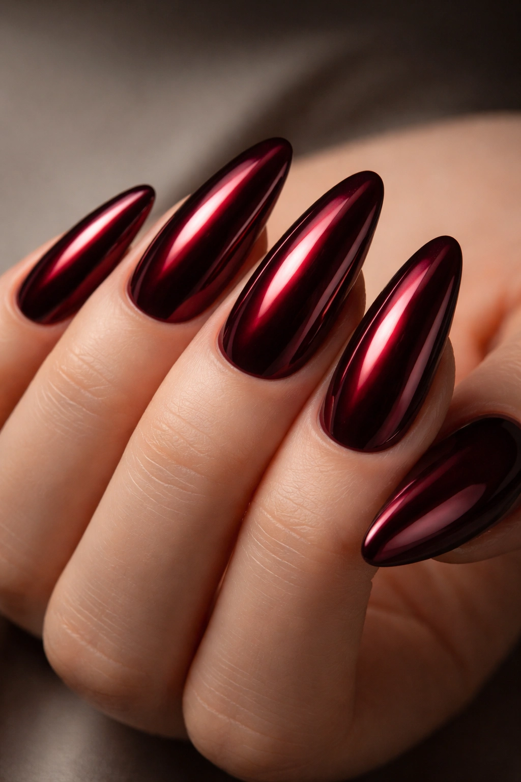 Close-up of dark cherry red chrome nails with reflective glossy finish.