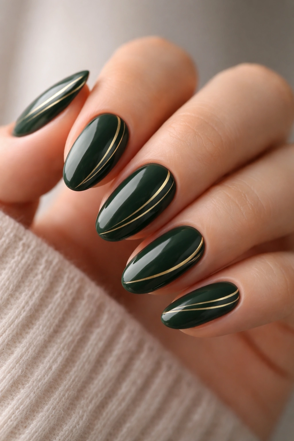 Close-up of short almond nails with deep green base and thin gold lines