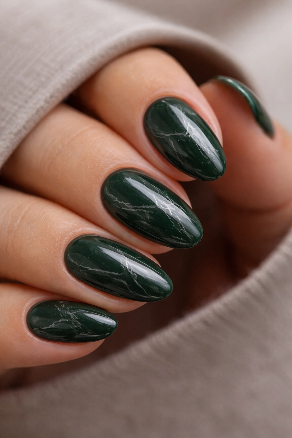 Close-up of dark green almond nails with subtle white veining