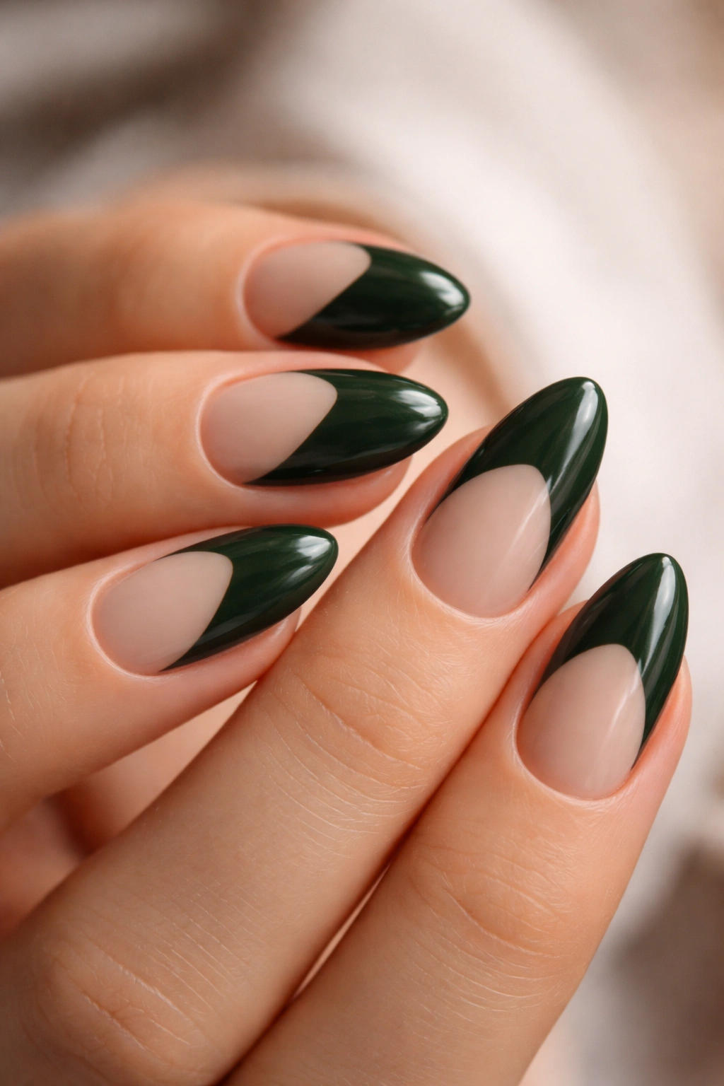 Close-up of short almond nails with dark green base and nude negative space