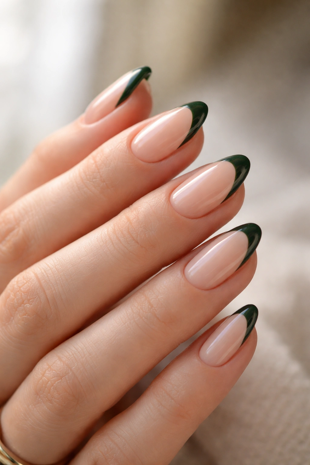 Close-up of short almond nails with nude base and dark green French tips, crisp and clean.