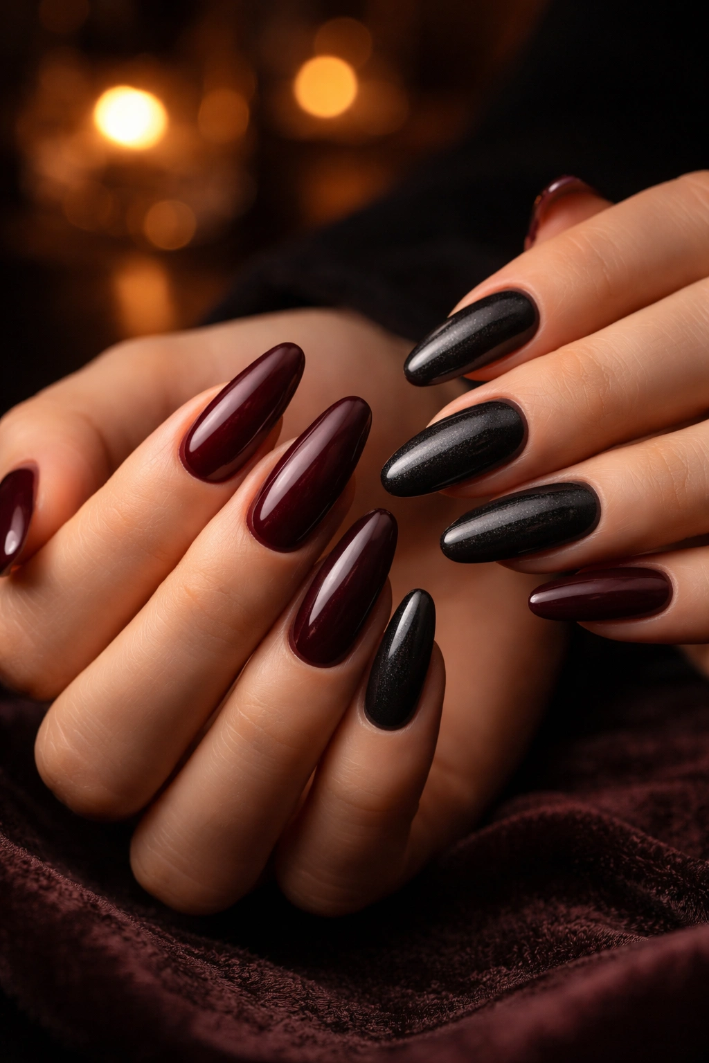 Close-up of hands with dark burgundy and charcoal nails under warm, dim lighting