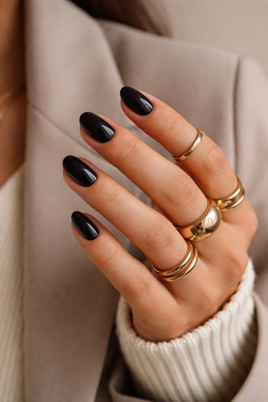 Hand with dark short oval nails and gold rings against neutral background