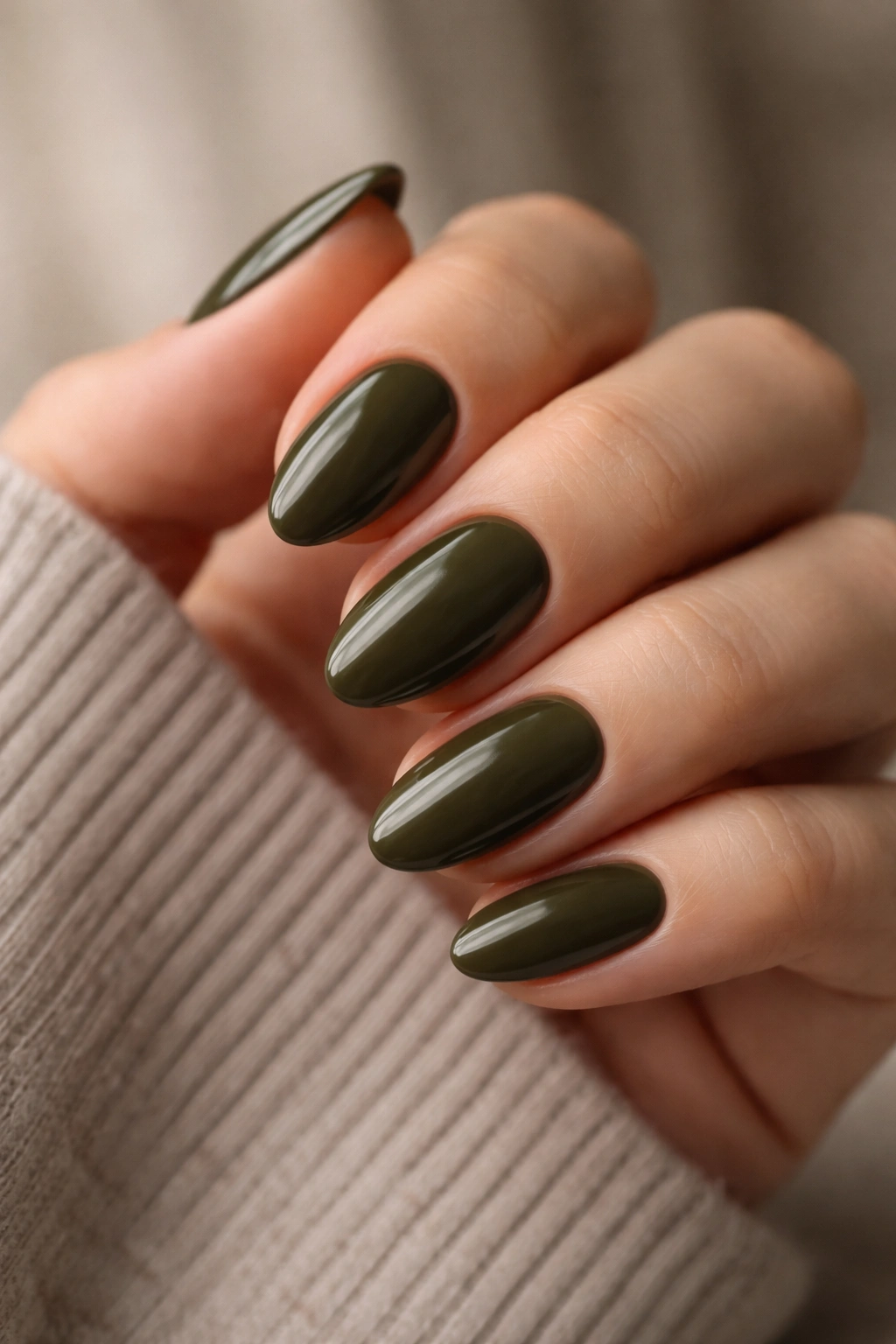Close-up of short almond nails painted dark olive with green-brown undertones on a neutral background