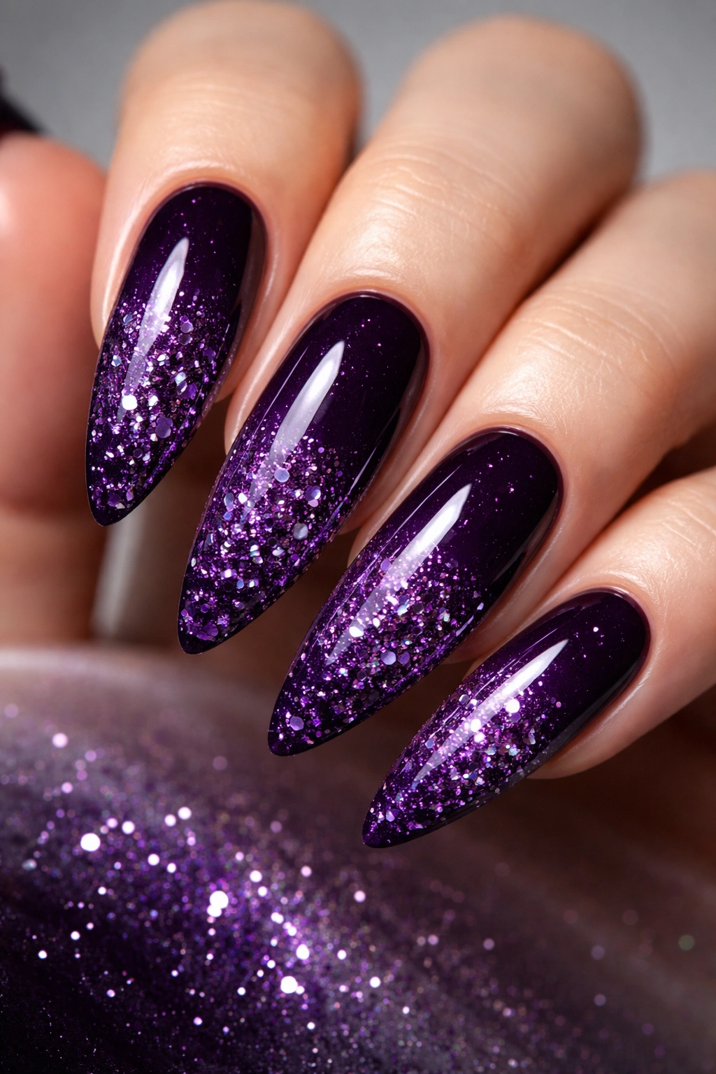 Close-up of long almond nails with dark purple glitter explosion at the tips