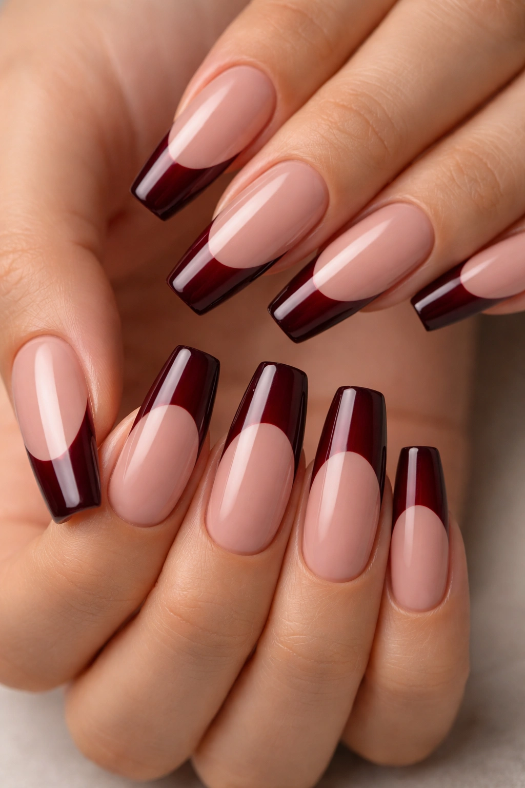 Close-up of coffin nails with nude base and dark red burgundy French tip, glossy finish