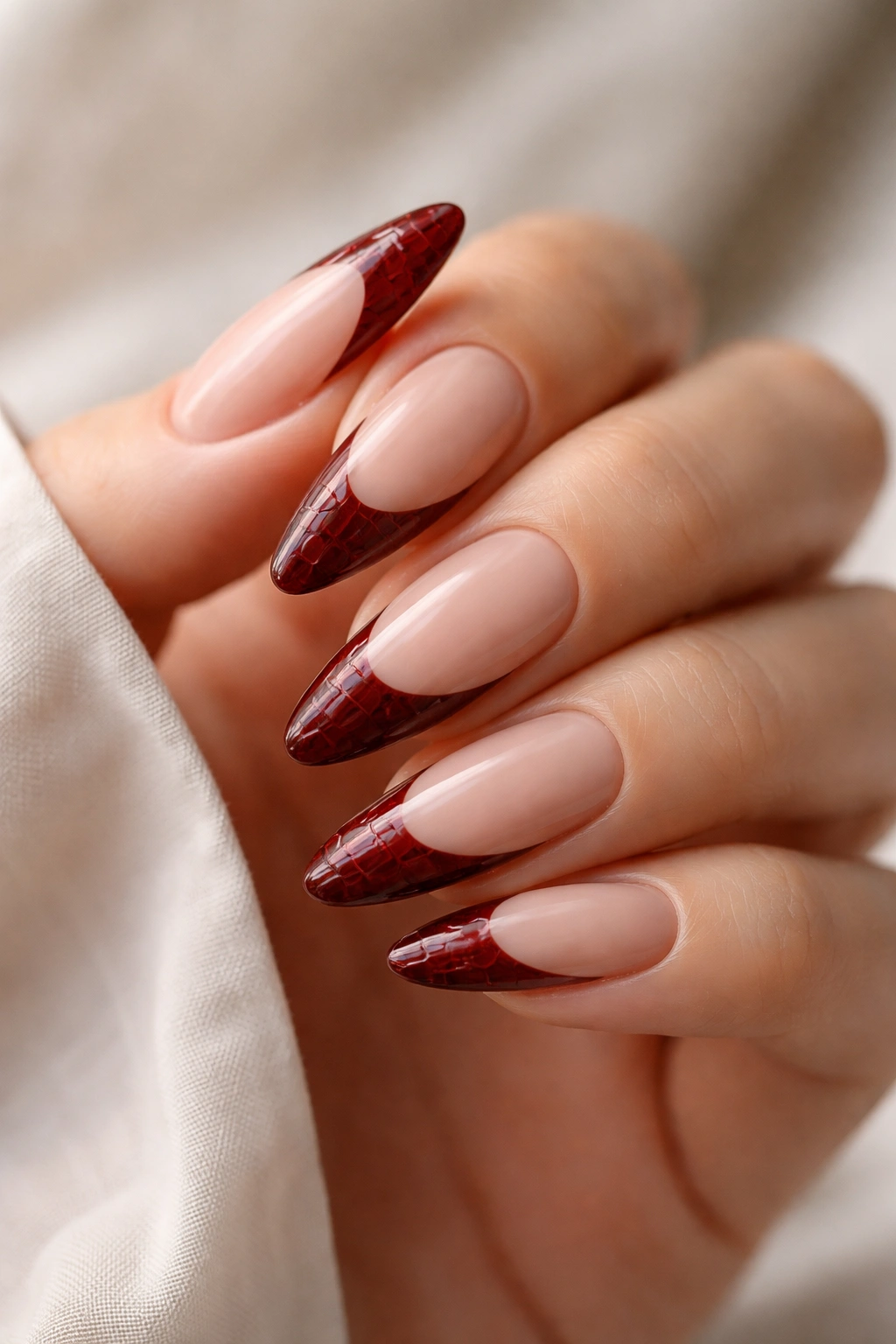 Close-up of almond nails with dark red croc-textured tips on nude base