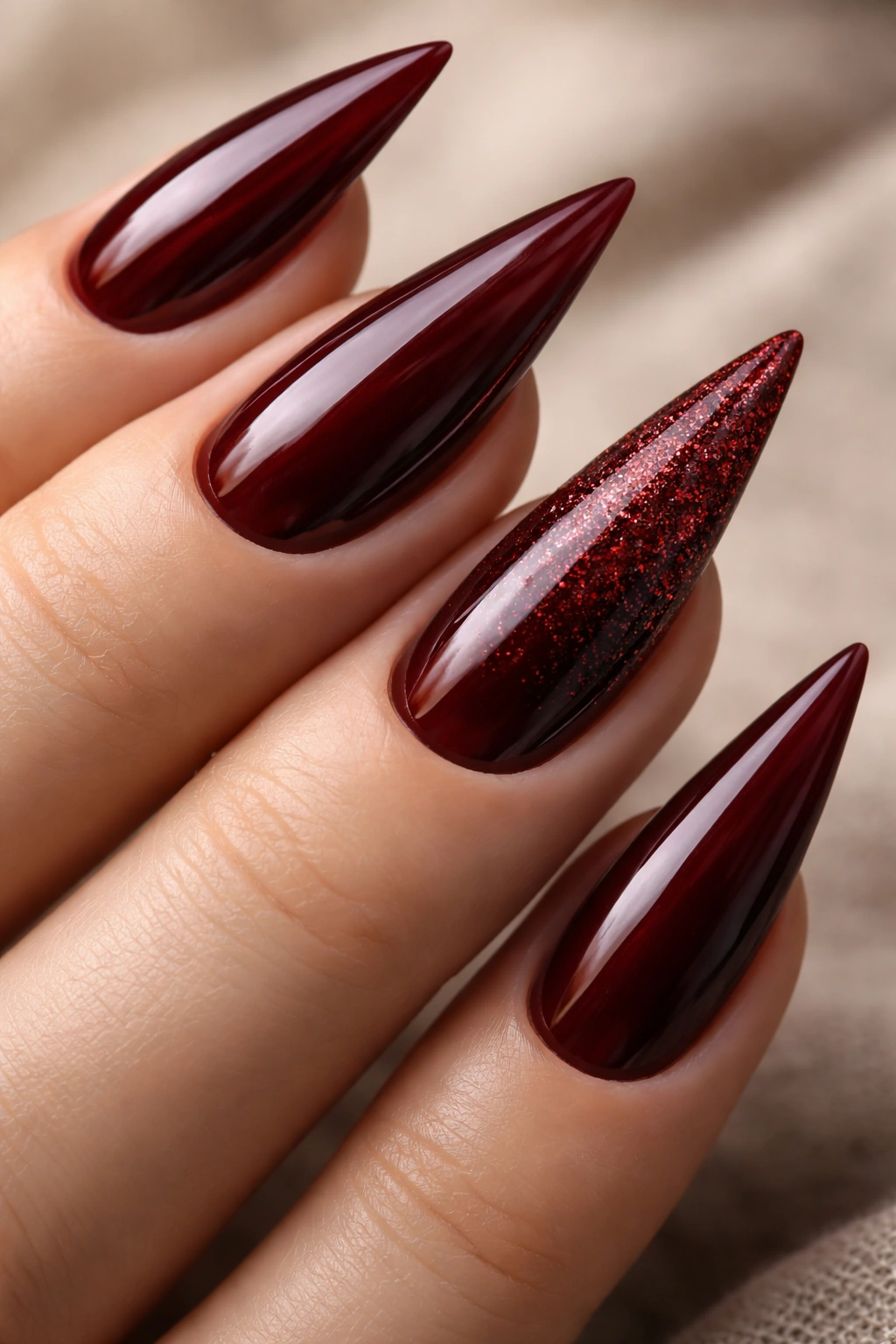 Close-up of dark red stiletto nails with glitter accents on a neutral background