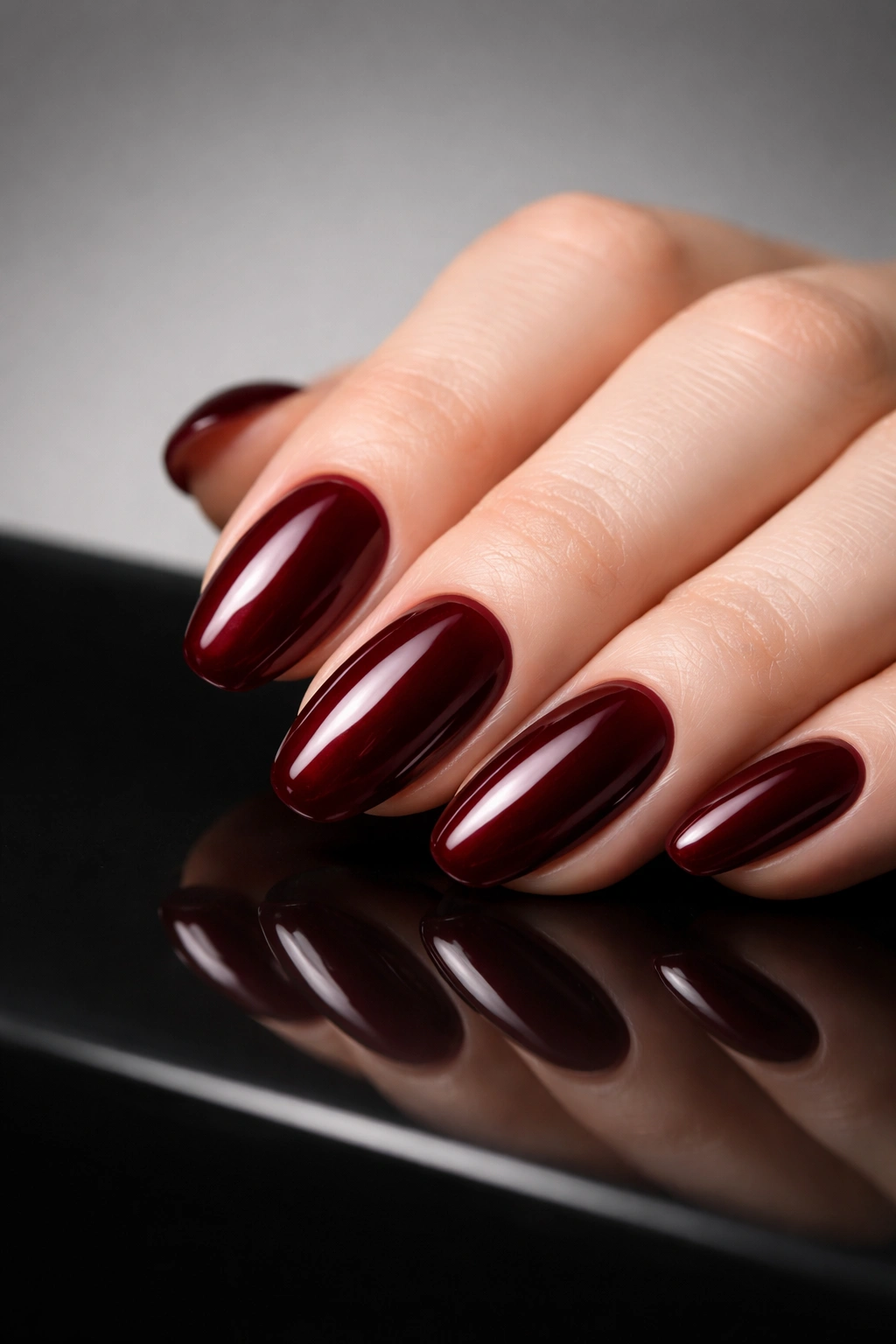 Close-up of a dark red glossy manicure on a single hand in a moody studio