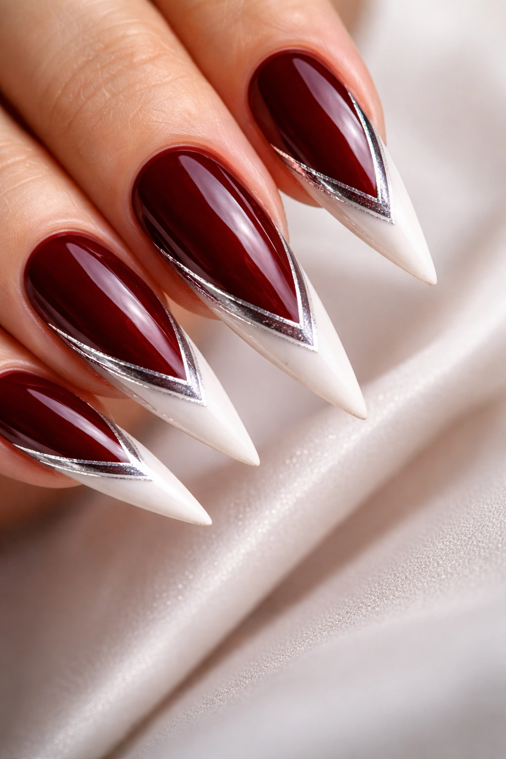 Stiletto nails with dark red base, white tips and silver accents