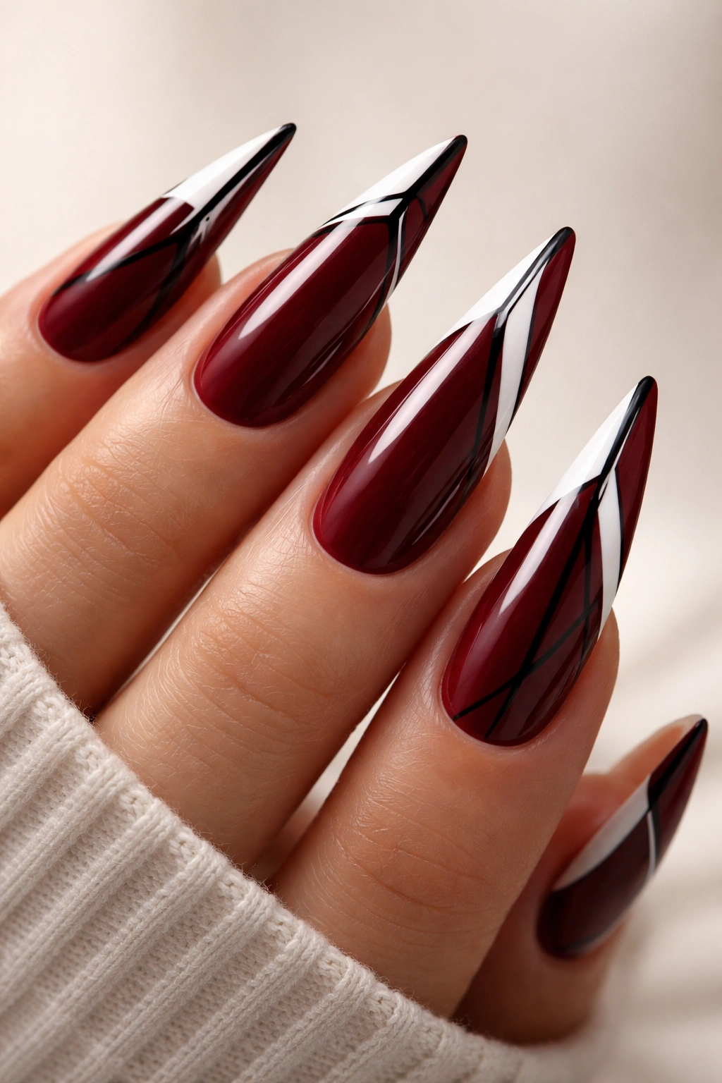 Close-up of dark red stiletto nails with white tips and black stripes