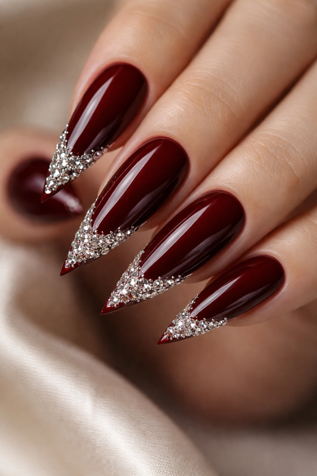 Close-up of dark red stiletto nails with rhinestones on the tips, high-detail
