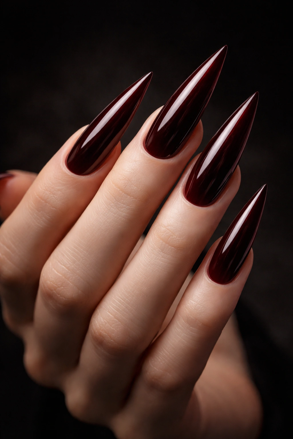 Dark red stiletto nails with glossy finish on a hand.