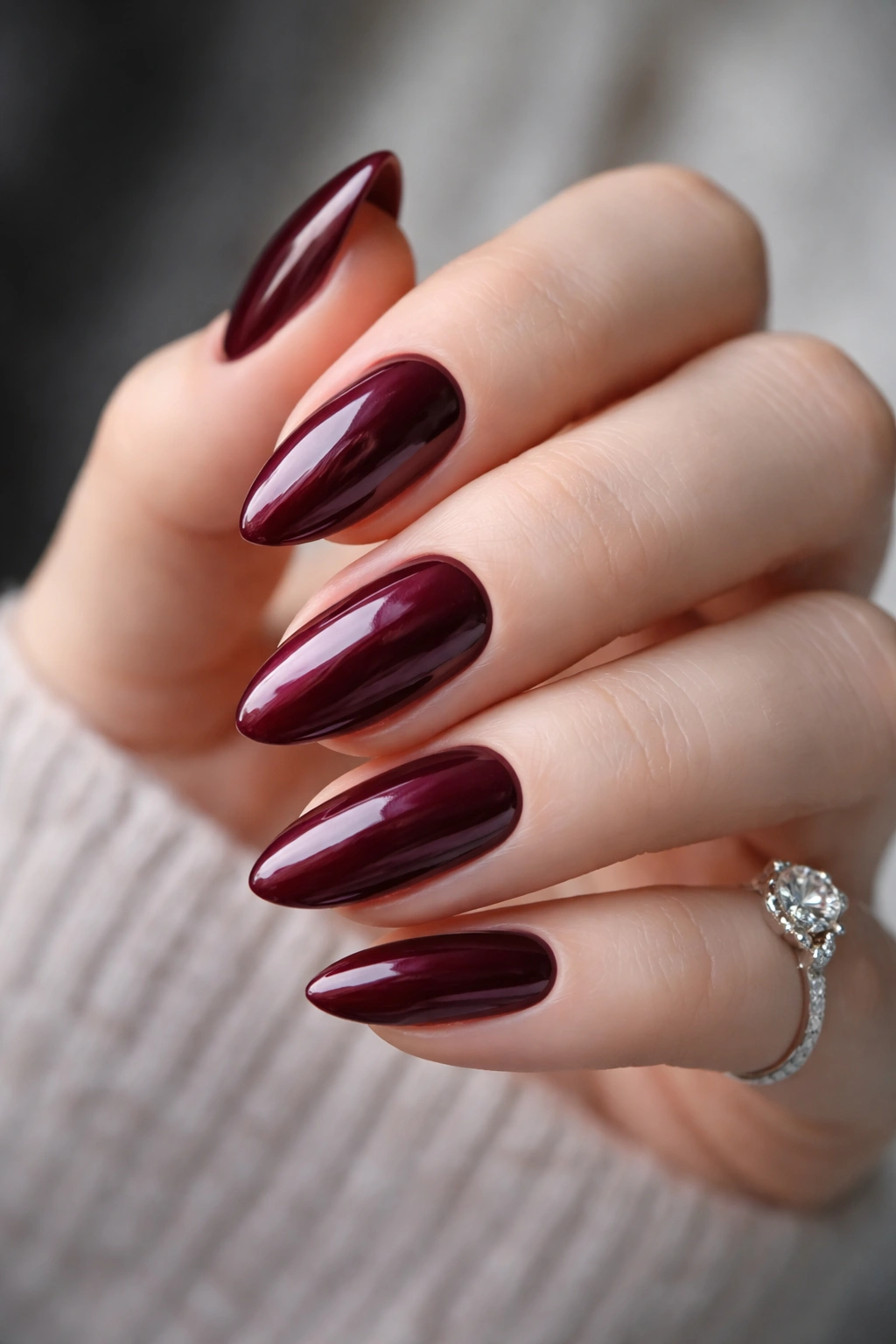 Close-up of deep berry burgundy nails on a hand with neutral background