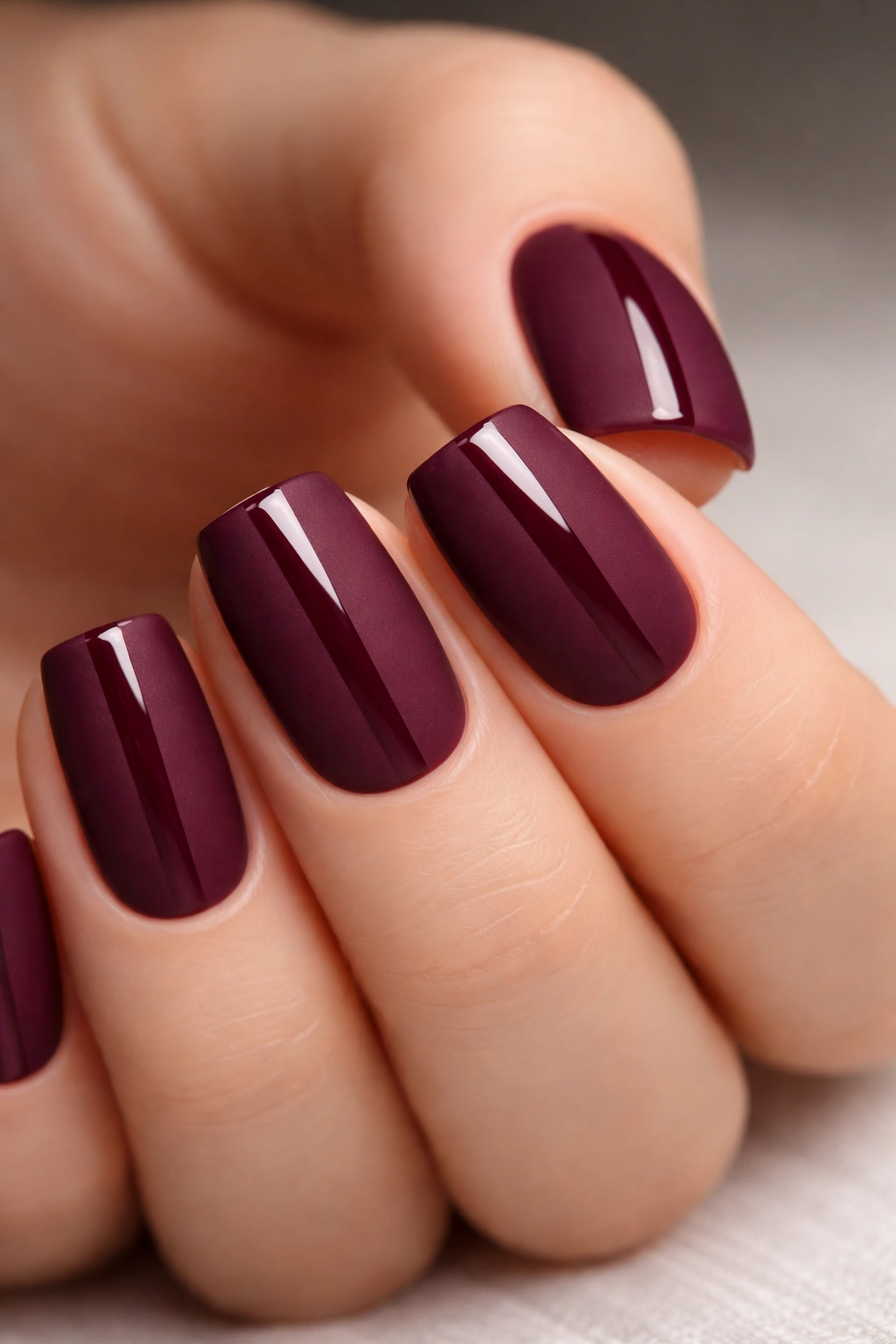 Close-up of short soft square nails in deep berry with matte base and glossy center stripe
