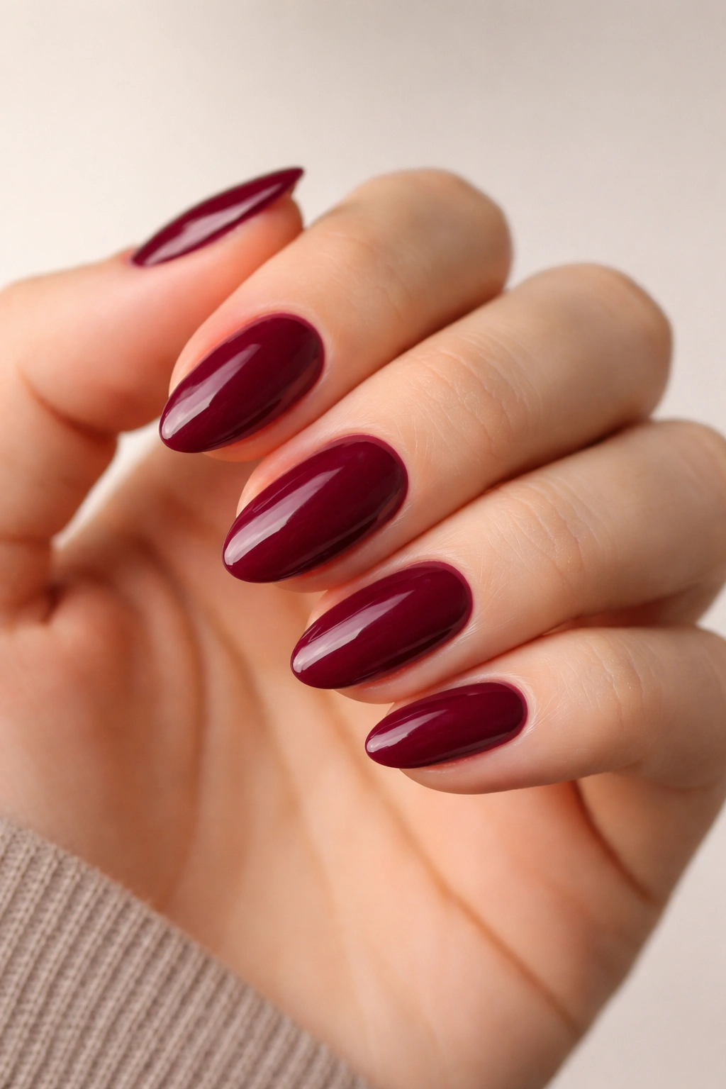 Close-up of deep berry short almond nails with glossy finish on neutral background