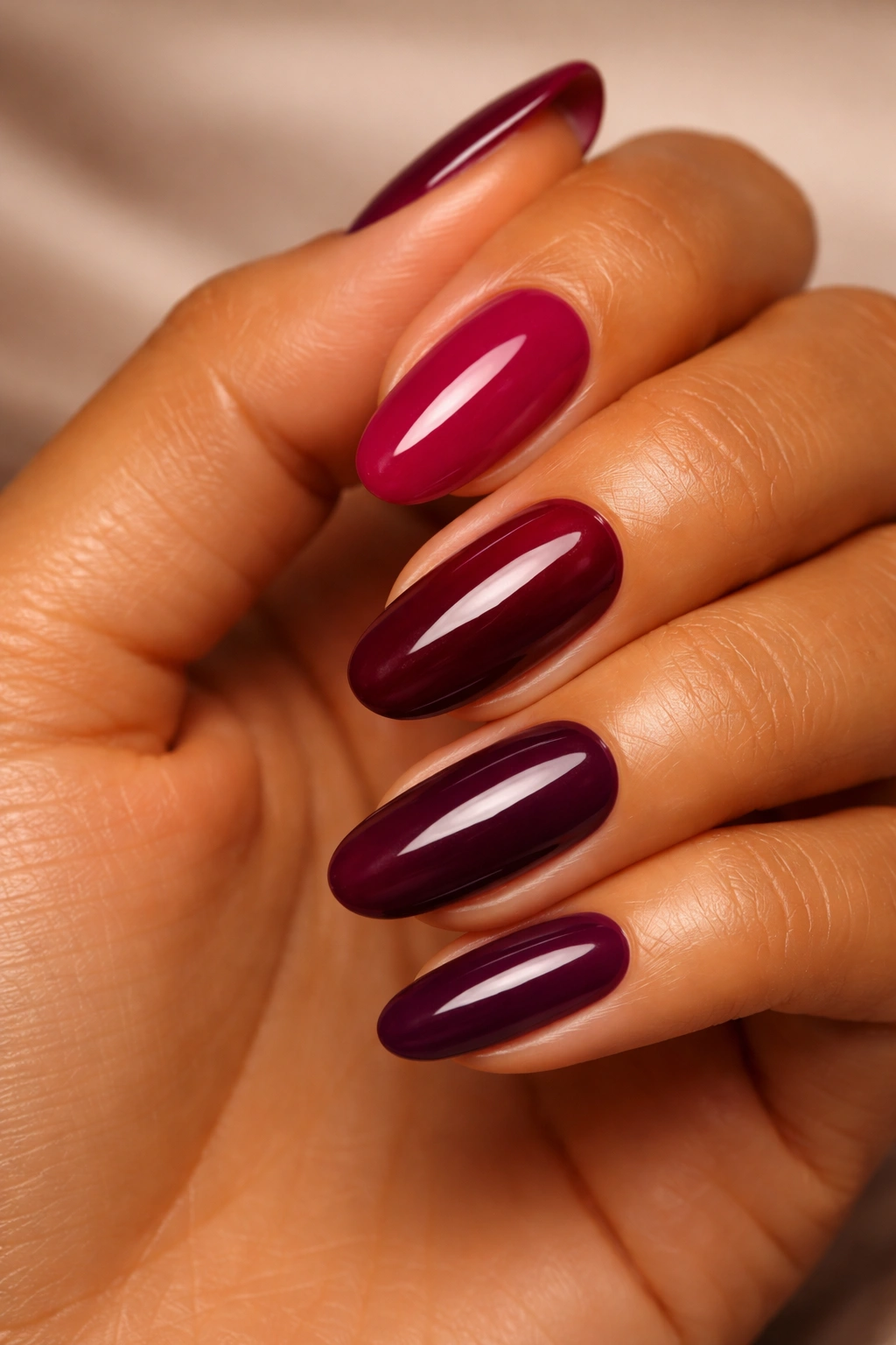 Close-up of a tanned hand with deep berry nail polish in raspberry, wine and burgundy tones.