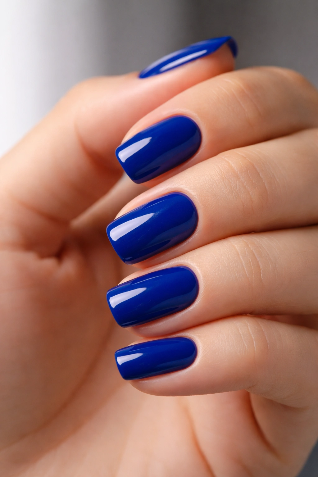 Close-up of short squoval nails painted deep saturated blue with a glossy finish