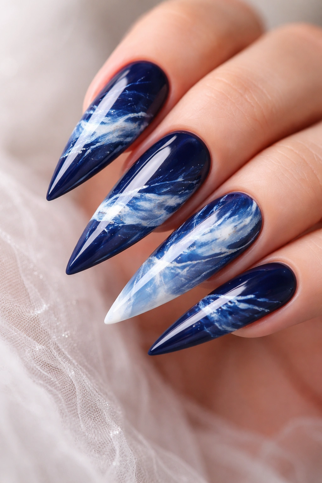 Deep blue stiletto nails with abstract white and pale blue watercolor patterns.
