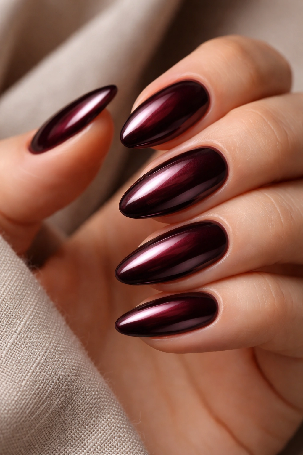 Close-up of short almond nails with deep burgundy chrome finish