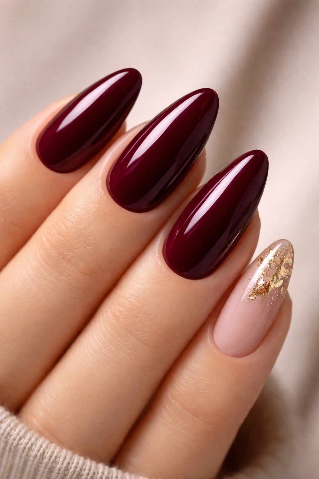 Close-up of deep burgundy nails with gold foil accent on one nail