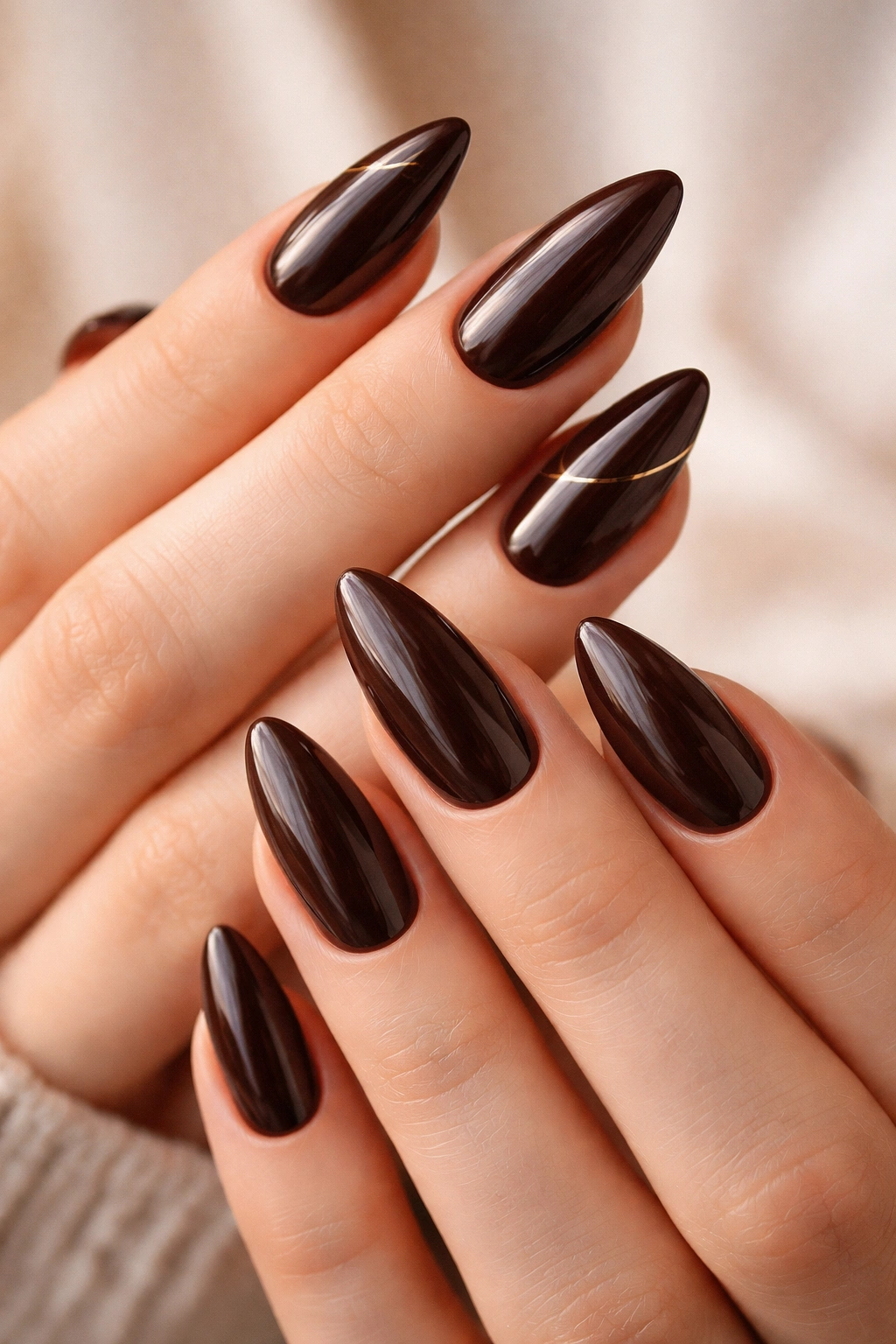 Close-up of deep chocolate almond nails with glossy finish and gold line